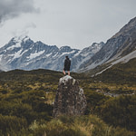 A man standing on the stone in Hooker Valley Track with a view of Mount Cook in New Zealand